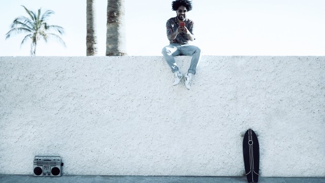 african-american-man-on-wall-with-smartphone-boombox-skateboard