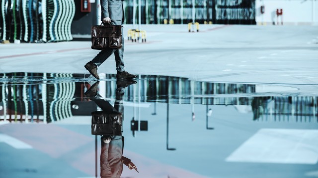 man-walks-with-suit-and-briefcase-reflection-in-puddle